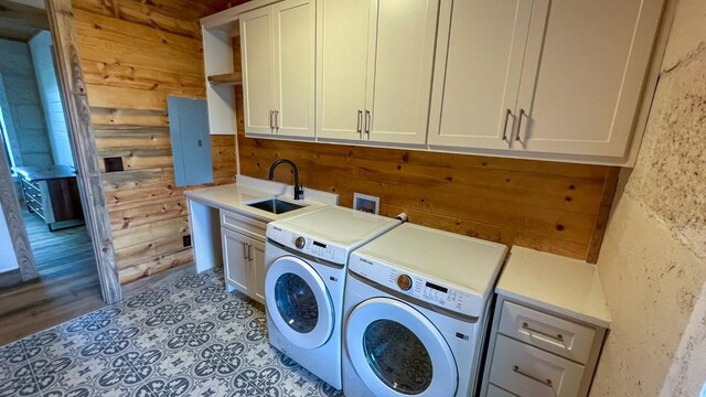 laundry area featuring wood walls, cabinets, sink, light wood-type flooring, and separate washer and dryer