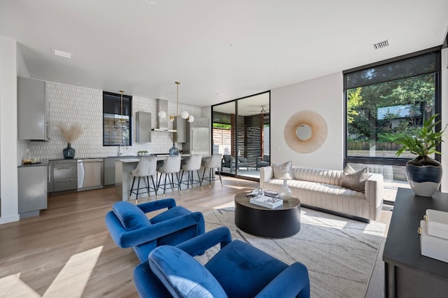 living room with plenty of natural light, ceiling fan, a wall of windows, and light hardwood / wood-style flooring