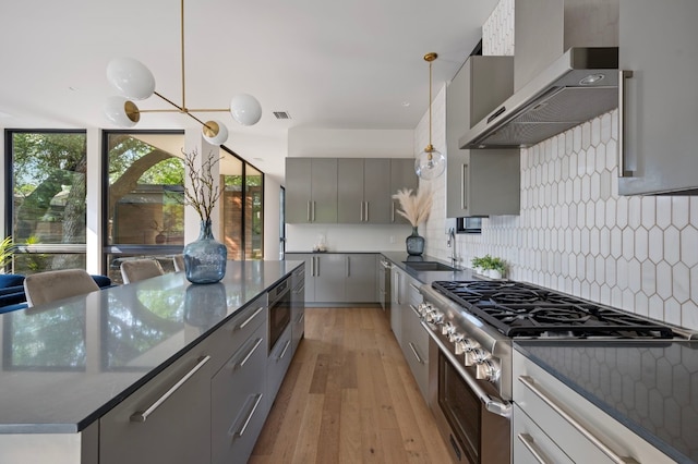 kitchen featuring light hardwood / wood-style floors, decorative light fixtures, wall chimney range hood, and appliances with stainless steel finishes