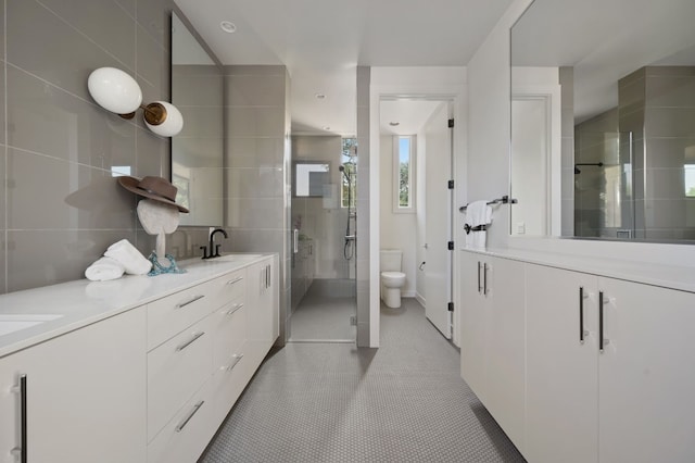 bathroom featuring vanity, a shower with door, tile patterned floors, toilet, and tile walls