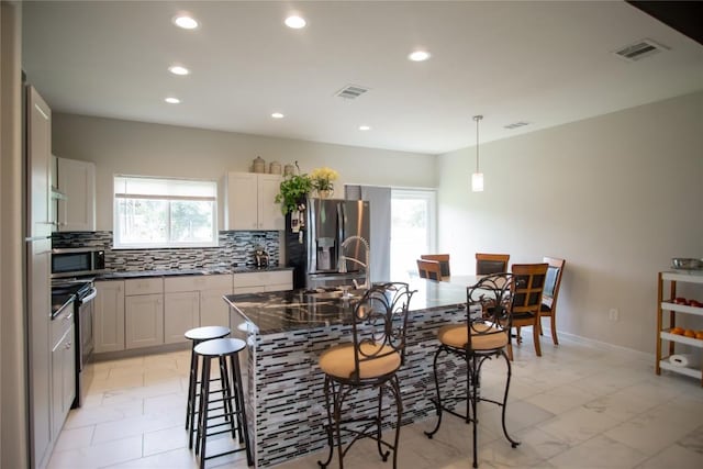 kitchen with pendant lighting, a healthy amount of sunlight, stainless steel appliances, and a kitchen island with sink