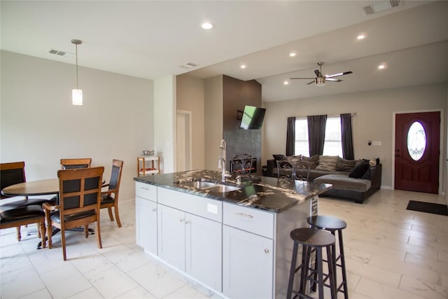 kitchen featuring white cabinets, sink, ceiling fan, dark stone countertops, and an island with sink