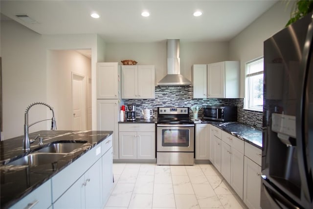 kitchen with white cabinetry, sink, stainless steel appliances, wall chimney range hood, and dark stone countertops