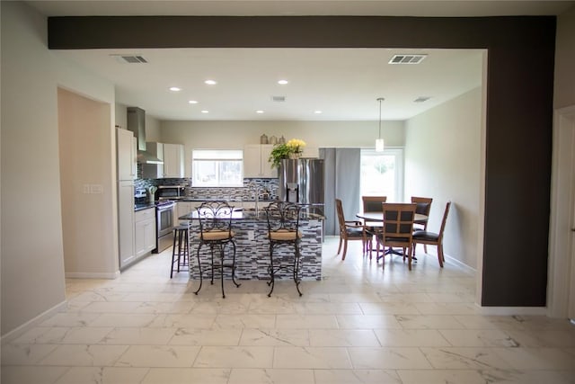 kitchen featuring backsplash, wall chimney exhaust hood, a healthy amount of sunlight, and appliances with stainless steel finishes