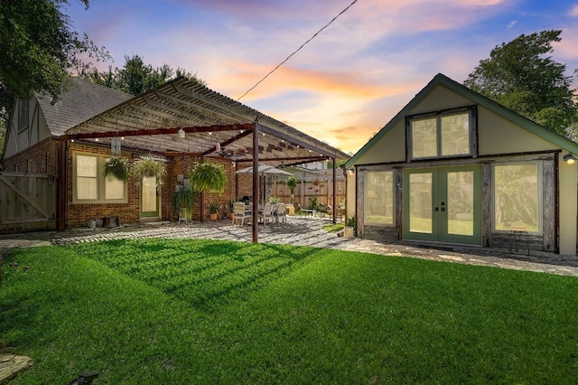 back house at dusk with a patio area, a yard, and french doors