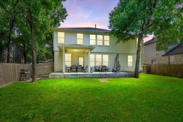 back house at dusk with a lawn and a patio area