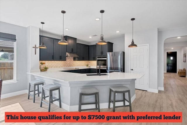 kitchen featuring backsplash, hanging light fixtures, appliances with stainless steel finishes, kitchen peninsula, and a breakfast bar area