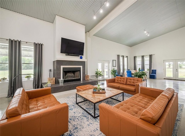 living room featuring beam ceiling, a tiled fireplace, french doors, and a towering ceiling