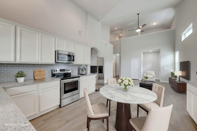 kitchen with appliances with stainless steel finishes, white cabinetry, high vaulted ceiling, and light hardwood / wood-style floors