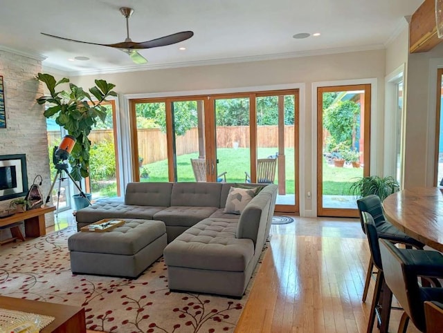 living room featuring ceiling fan, a stone fireplace, crown molding, and light hardwood / wood-style flooring