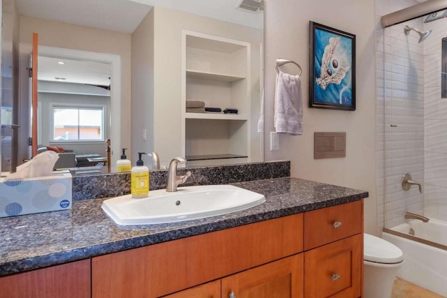 full bathroom featuring shower / bath combination with glass door, built in shelves, vanity, and toilet