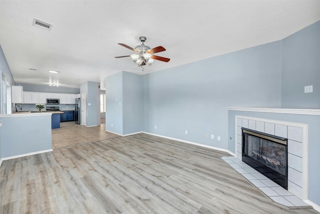 unfurnished living room with light wood-type flooring, sink, a tile fireplace, and ceiling fan