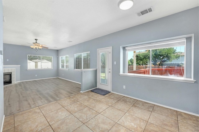 unfurnished living room with light wood-type flooring, a wealth of natural light, ceiling fan, and a fireplace