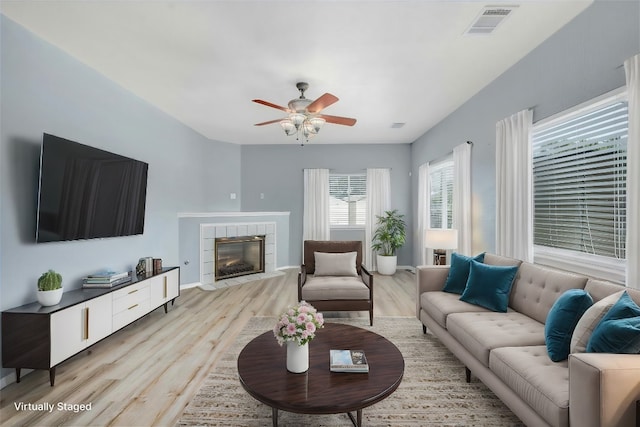 living room with light wood-type flooring, a tile fireplace, and ceiling fan