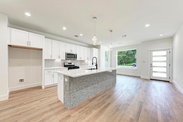 kitchen featuring white cabinetry, hanging light fixtures, stainless steel appliances, a kitchen island with sink, and light wood-type flooring