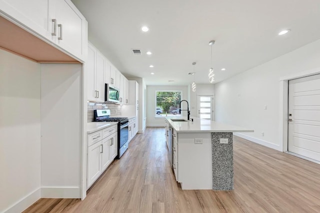 kitchen featuring stainless steel appliances, white cabinetry, hanging light fixtures, and a center island with sink