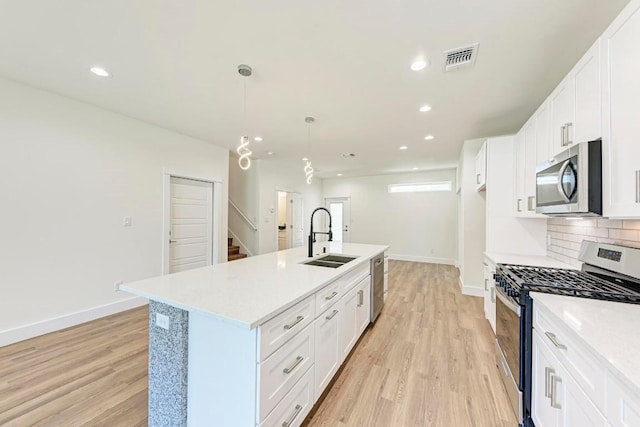 kitchen featuring a kitchen island with sink, white cabinets, sink, light hardwood / wood-style flooring, and appliances with stainless steel finishes