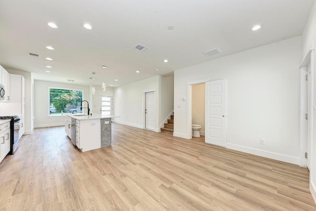 kitchen featuring pendant lighting, a center island with sink, white cabinets, light hardwood / wood-style flooring, and gas stove