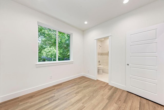 unfurnished bedroom featuring ensuite bath and light hardwood / wood-style floors