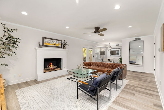 living room featuring crown molding, ceiling fan, a brick fireplace, and light hardwood / wood-style flooring