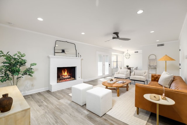 living room featuring a brick fireplace, light wood-type flooring, ceiling fan, and ornamental molding