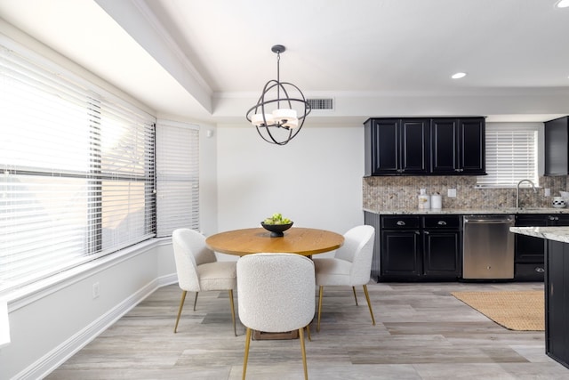 dining area featuring sink, a chandelier, ornamental molding, a tray ceiling, and light wood-type flooring