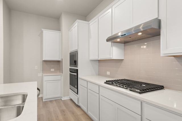 kitchen with appliances with stainless steel finishes, extractor fan, white cabinetry, decorative backsplash, and light wood-type flooring