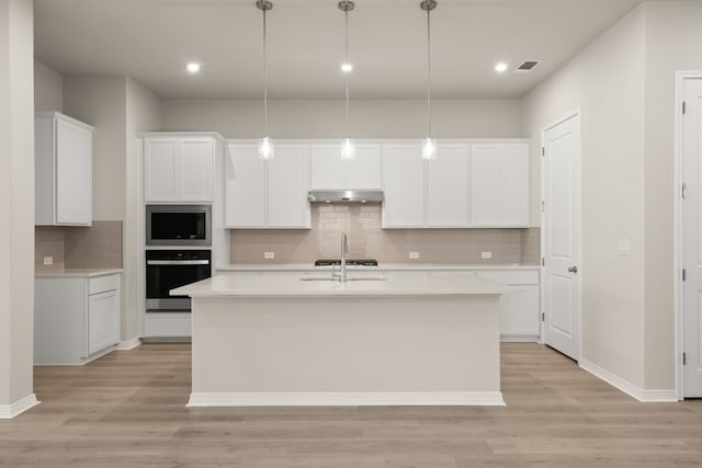 kitchen with decorative light fixtures, white cabinetry, a kitchen island with sink, stainless steel oven, and built in microwave