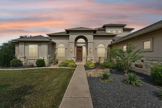 view of front of property featuring stone siding, a yard, and stucco siding