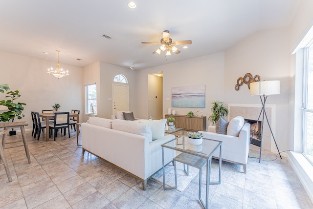 living room featuring ceiling fan with notable chandelier, plenty of natural light, and a tiled fireplace