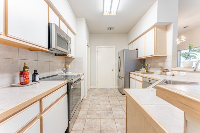 kitchen with decorative backsplash, light tile patterned floors, tile counters, white cabinetry, and stainless steel appliances