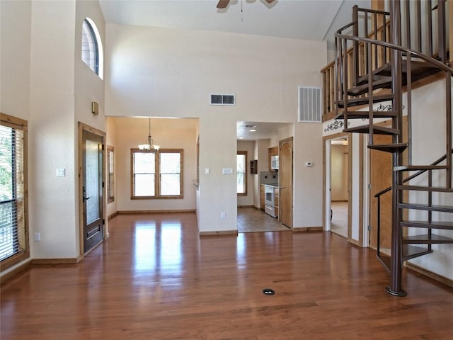 unfurnished living room featuring ceiling fan with notable chandelier, dark hardwood / wood-style floors, and high vaulted ceiling