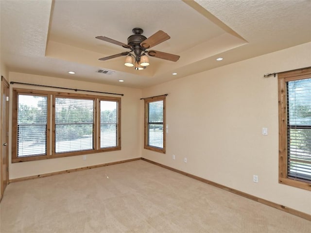 carpeted spare room with a textured ceiling, a tray ceiling, and ceiling fan