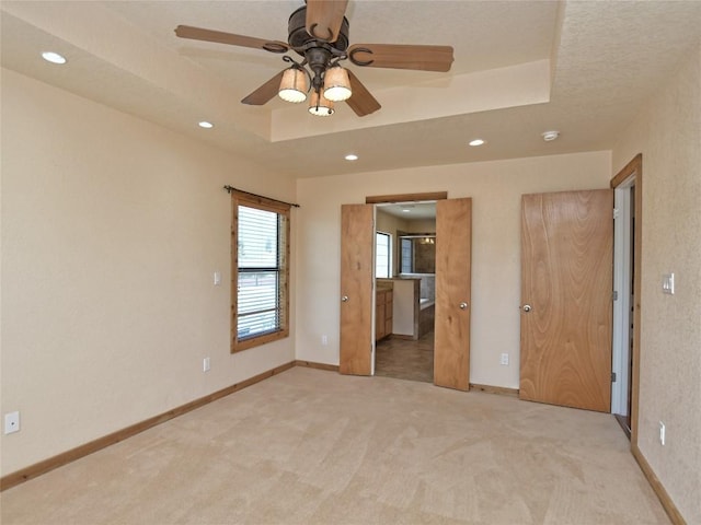 unfurnished bedroom featuring a tray ceiling, connected bathroom, ceiling fan, and light colored carpet