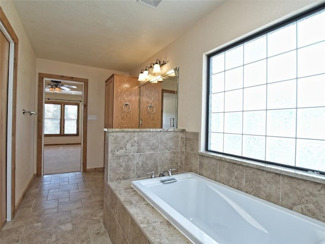 bathroom featuring ceiling fan, tiled tub, and a wealth of natural light