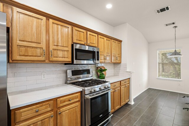 kitchen featuring light stone counters, stainless steel appliances, backsplash, dark tile flooring, and pendant lighting