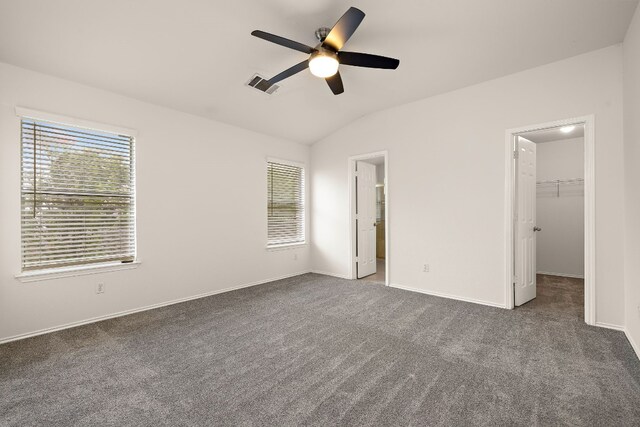 unfurnished bedroom with ceiling fan, vaulted ceiling, dark carpet, and a spacious closet