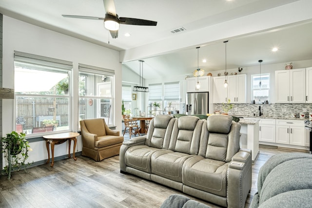 living room with ceiling fan, light wood-type flooring, lofted ceiling with beams, and sink