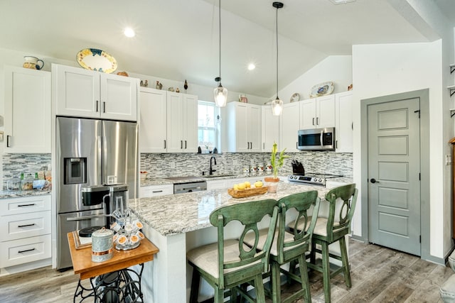 kitchen with vaulted ceiling, stainless steel appliances, a center island, light stone counters, and white cabinets