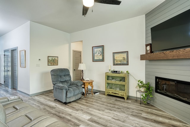 living area featuring ceiling fan, a large fireplace, and light hardwood / wood-style floors