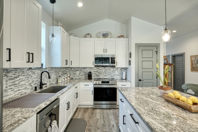 kitchen featuring appliances with stainless steel finishes, hanging light fixtures, white cabinets, lofted ceiling, and sink