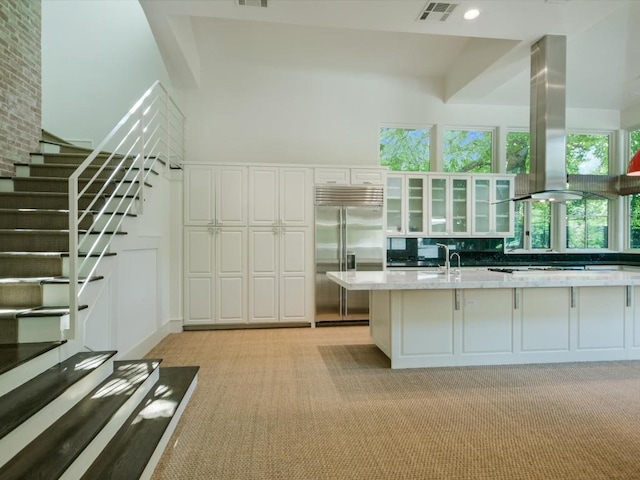 kitchen featuring white cabinets, built in refrigerator, light stone countertops, island range hood, and light colored carpet