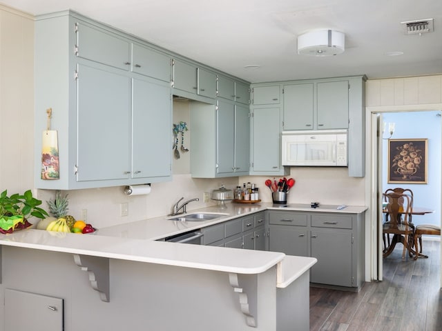 kitchen featuring dishwasher, sink, dark hardwood / wood-style flooring, kitchen peninsula, and a breakfast bar area