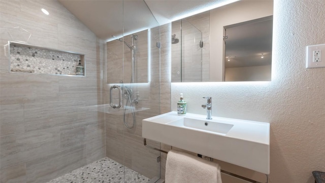 full bath featuring vaulted ceiling, a textured wall, a stall shower, and a sink