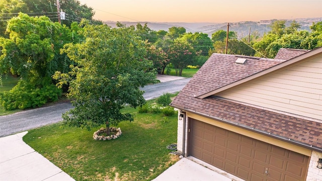 exterior space featuring a garage, driveway, a shingled roof, and a lawn