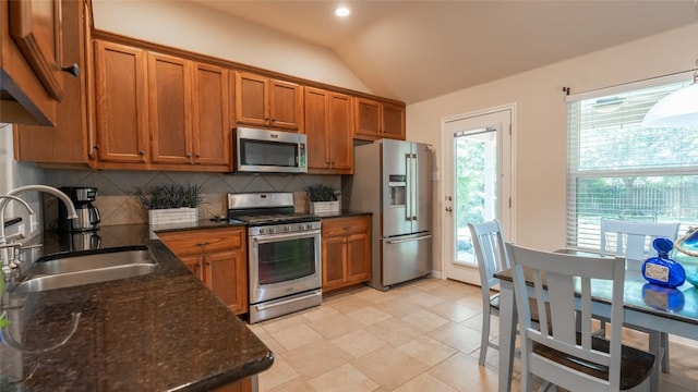 kitchen with brown cabinetry, lofted ceiling, a sink, stainless steel appliances, and backsplash