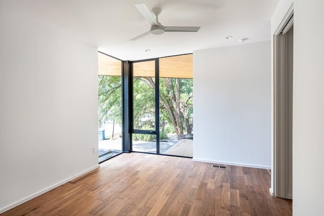 unfurnished room featuring wood-type flooring, a wall of windows, and ceiling fan