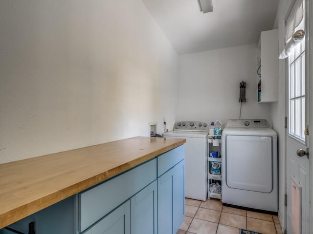 clothes washing area with washing machine and clothes dryer, light tile patterned floors, and cabinets