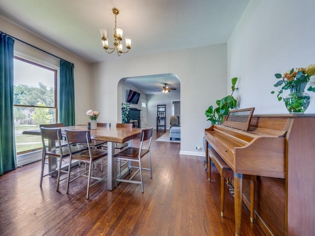 dining space featuring ceiling fan with notable chandelier, dark hardwood / wood-style flooring, and a fireplace