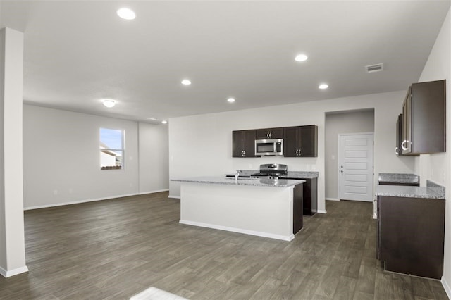 kitchen featuring dark wood-type flooring, a kitchen island with sink, appliances with stainless steel finishes, and light stone counters